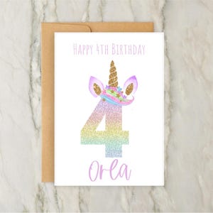 May include: A birthday card with a unicorn theme. The card features the text "Happy 4th Birthday" above a large number "4" in a rainbow glitter design. The card also includes the name "Orea" in a script font.