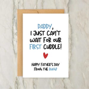 Puede incluir: Una tarjeta blanca del Día del Padre con el texto "Daddy, I just can't wait for our first cuddle!" en fuente azul y negra, con un corazón rojo. La tarjeta está en un sobre marrón. El texto "Happy Father's Day from the bump" también está en la tarjeta.