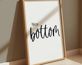 May include: A rectangular wall art print in a light-toned wooden frame. The print features a white background with the text Nice bottom printed in black ink. The word Nice is in a simple sans-serif font, while bottom is in a cursive script.