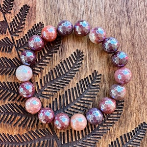 May include: A bracelet made of faceted agate beads in shades of brown, pink, and purple. The beads are arranged in a circular pattern and have a glossy finish.