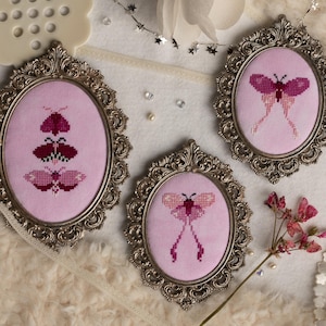 May include: Three ornate oval frames with pink backgrounds and embroidered pink and red butterflies. The frames are silver and have a decorative design.