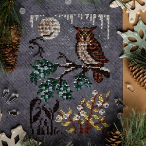 May include: A cross-stitch pattern of an owl perched on a branch with a full moon in the background. The owl is brown and white with yellow eyes. The branch is surrounded by green and blue leaves. The moon is white with a brown center. The background is a dark blue.