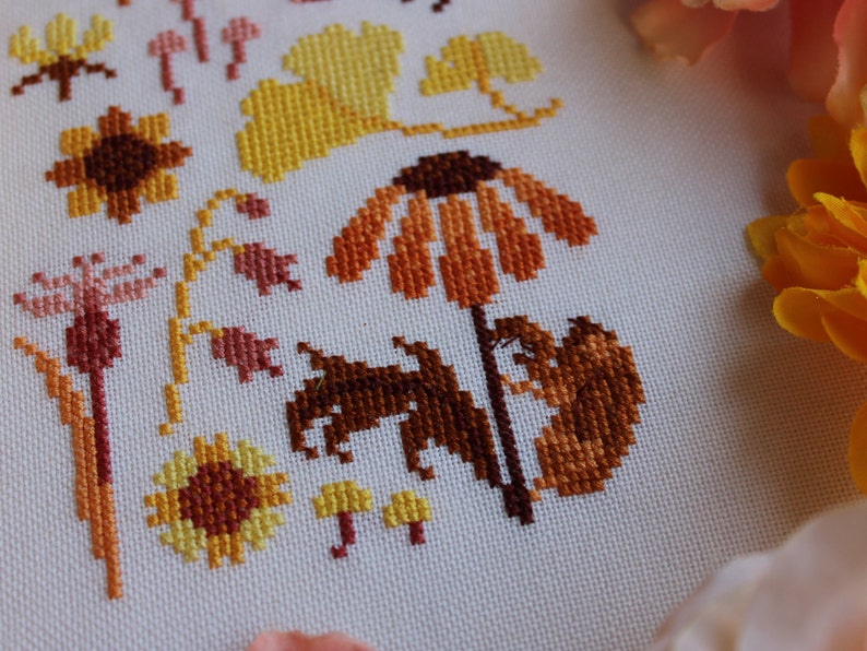 Peut inclure: Broderie au point de croix repr&eacute;sentant une vari&eacute;t&eacute; de fleurs et de feuilles d'automne dans des tons d'orange, de jaune et de brun. Le motif comprend des tournesols, des marguerites et des feuilles.