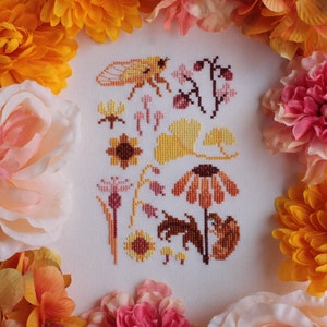 Peut inclure: Broderie au point de croix repr&eacute;sentant une vari&eacute;t&eacute; de motifs floraux et d'insectes dans des tons de jaune, orange et marron. Le motif comprend une cigale, des tournesols, des feuilles de ginkgo et d'autres fleurs.