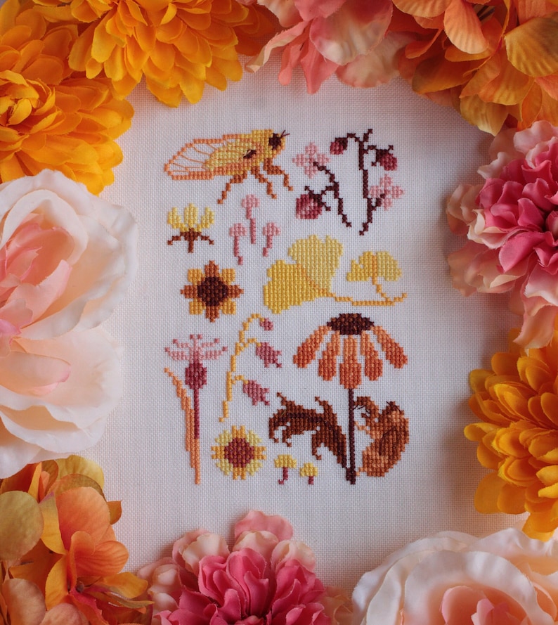 Peut inclure: Broderie au point de croix repr&eacute;sentant une vari&eacute;t&eacute; de motifs floraux et d'insectes dans des tons de jaune, orange et marron. Le motif comprend une cigale, des tournesols, des feuilles de ginkgo et d'autres fleurs.