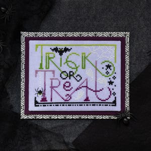 Puede incluir: Un diseño de punto de cruz con las palabras "Trick or Treat" en verde, blanco y morado. Un murciélago y una araña negros están incluidos en el diseño. El diseño está enmarcado con un patrón geométrico y sobre un fondo oscuro con arañas de plástico.
