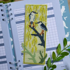 May include: A rectangular needlepoint bookmark featuring two birds perched on a dark blue branch against a background of yellow willow leaves. The design is stitched on a light-colored grid canvas with a green border and green branch at the base.