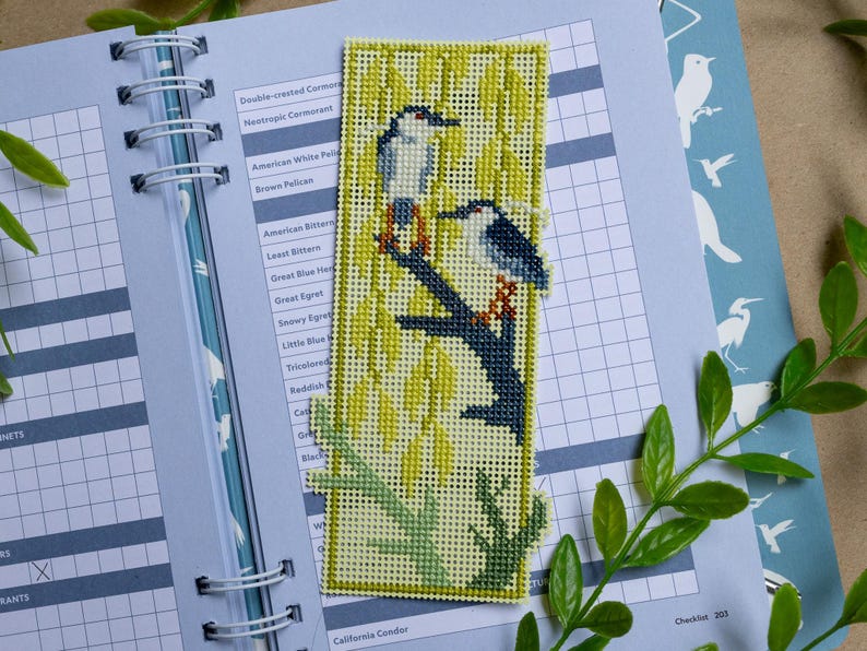 May include: A rectangular needlepoint bookmark featuring two birds perched on a dark blue branch against a background of yellow willow leaves. The design is stitched on a light-colored grid canvas with a green border and green branch at the base.