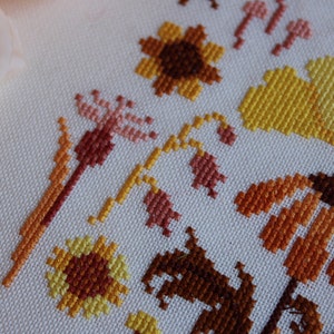 Peut inclure: Gros plan sur une broderie au point de croix repr&eacute;sentant une vari&eacute;t&eacute; de fleurs dans des tons de jaune, orange et marron. Les fleurs sont brod&eacute;es sur un fond de tissu blanc.