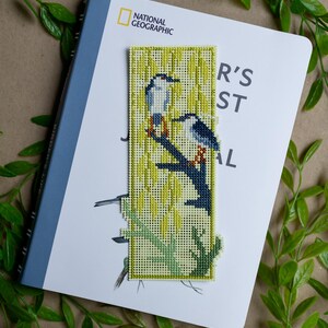 May include: A rectangular cross-stitch bookmark featuring two birds perched on a dark blue branch against a background of yellow willow leaves. The needlepoint design is stitched on a light yellow grid fabric with a distinct border and textured finish.