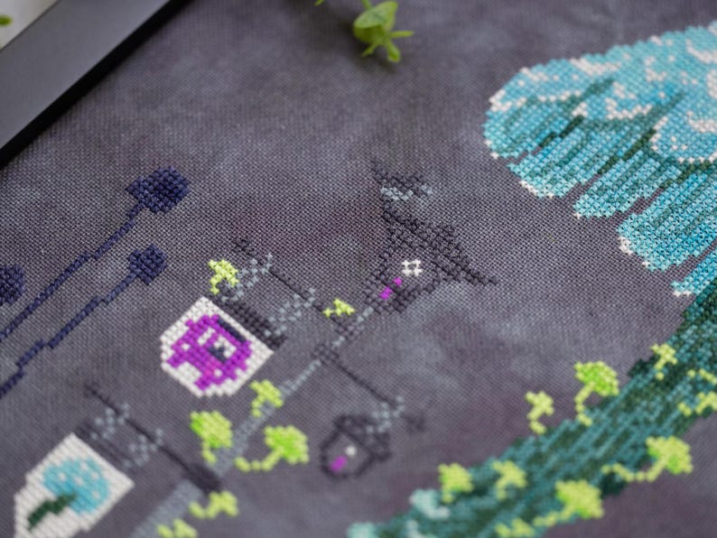 May include: Cross-stitch artwork featuring a nighttime scene with street lamps, a building, and stylized floral elements. The lamps have purple and white accents, and the overall color palette includes shades of gray, purple, green, and blue.