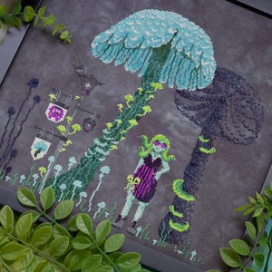 May include: Cross-stitch art featuring a fantasy scene with large mushrooms in shades of blue and green. A figure with green hair and sunglasses stands near the mushrooms. The artwork is framed in a black frame.