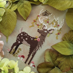 May include: A cross-stitch design of a deer with white spots and antlers, adorned with flowers and berries. The deer is surrounded by greenery and mushrooms, creating a woodland theme. The antlers have a spider web design.