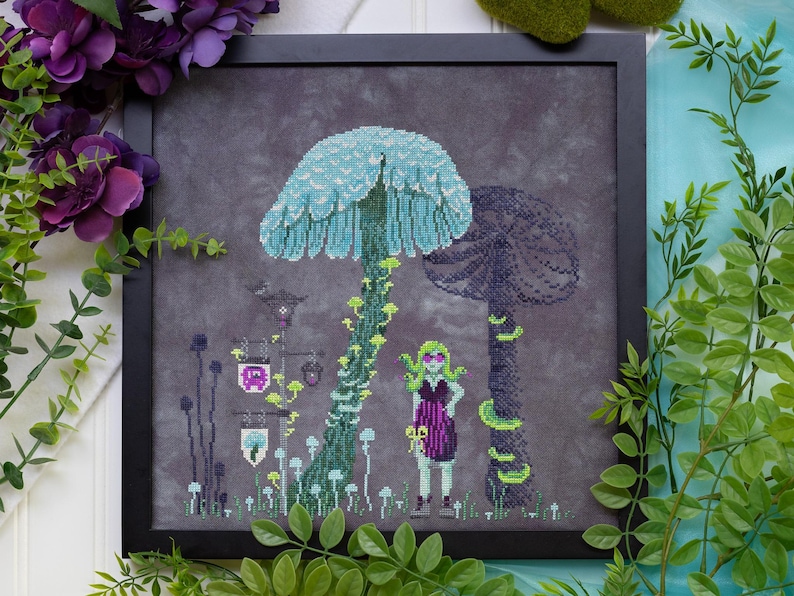 May include: Cross-stitch art in a black frame depicts a fantasy scene with large mushrooms, a figure, and stylized plants. The mushrooms are teal and purple, with a figure in a purple dress. The background is a dark gray.