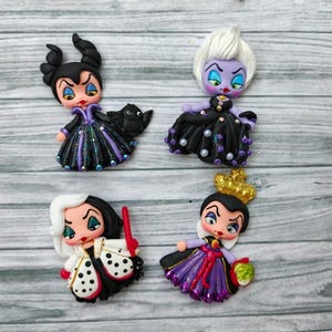 Peut inclure: Quatre figurines faites à la main de méchants Disney : Maléfique, Ursula, Cruella d'Enfer et la Méchante Reine. Chaque figurine est aux couleurs vives avec des détails complexes, notamment des costumes et des accessoires. Les figurines sont disposées sur une surface en bois gris clair.