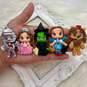 May include: A collection of five miniature figurines inspired by characters from The Wizard of Oz. The figurines include the Tin Man, a princess, the Wicked Witch, Dorothy, and the Cowardly Lion. Each figure is brightly colored and detailed.