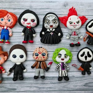 Puede incluir: Una colección de figuras coloridas hechas a mano que representan personajes de películas de terror. Las figuras incluyen a Chucky, Jigsaw, The Nun, Pennywise, Ghostface, Freddy Krueger, Michael Myers, Jason Voorhees, Beetlejuice y otro Ghostface.