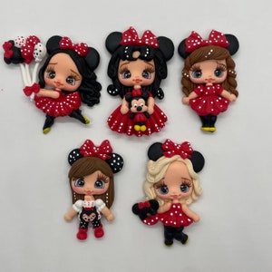 Puede incluir: Cinco figuras hechas a mano de un personaje de dibujos animados con grandes orejas negras y un lazo rojo de lunares. Las figuras visten vestidos rojos y sostienen globos o un peluche. Las figuras tienen diferentes colores y estilos de cabello.
