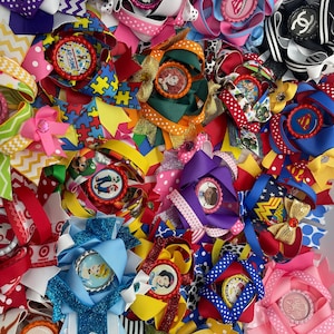May include: A collection of colorful hair bows with various designs and characters. The bows are made with different types of ribbon and feature a variety of centerpieces, including cartoon characters, logos, and words.