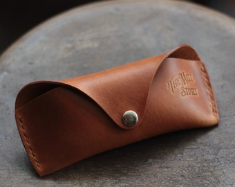 May include: A brown leather glasses case with a silver button closure. The case is embossed with the text "The Mill Story".