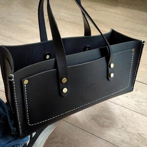 Puede incluir: Bolso tote de cuero negro con dos asas y un bolsillo delantero. El bolso presenta costuras blancas, remaches dorados y un peque&ntilde;o logotipo en relieve. El bolso est&aacute; dise&ntilde;ado con una parte superior abierta y una forma estructurada.