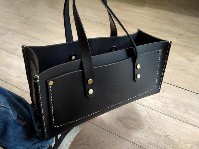 Puede incluir: Bolso tote de cuero negro con dos asas y un bolsillo delantero. El bolso presenta costuras blancas, remaches dorados y un peque&ntilde;o logotipo en relieve. El bolso est&aacute; dise&ntilde;ado con una parte superior abierta y una forma estructurada.