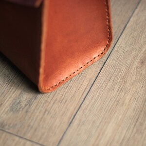 May include: Close-up of the bottom corner of a brown leather bag with stitching detail.