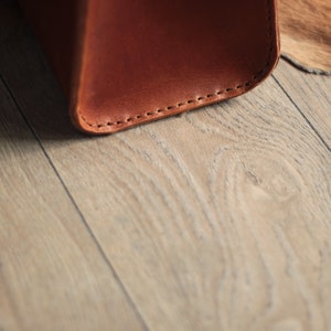 May include: Close-up of the bottom edge of a brown leather bag with visible stitching.