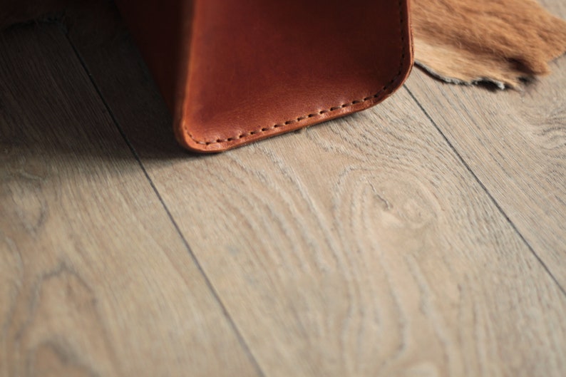 May include: Close-up of the bottom edge of a brown leather bag with visible stitching.