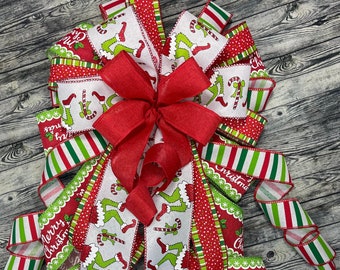 May include: A festive Christmas bow featuring a large red bow at the center. The bow is made of various ribbons with red, green, and white patterns, including stripes, polka dots, and a design with a cartoon character and candy canes. The words "Merry Christmas" are also visible.