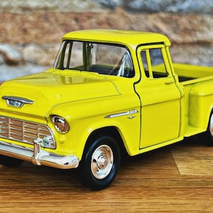 Puede incluir: Un modelo de camioneta vintage de color amarillo brillante. El juguete presenta una parrilla cromada detallada, faros y un diseño clásico. La camioneta mide aproximadamente 20 cm de largo.