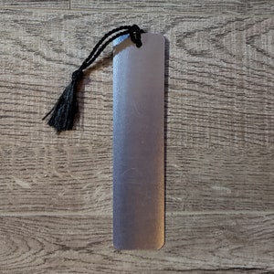 Puede incluir: Un marcap&aacute;ginas de metal plateado con un borla negra. El marcap&aacute;ginas est&aacute; sobre una superficie de madera.