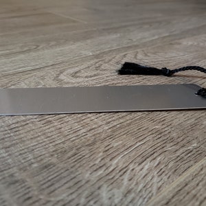 Puede incluir: Un marcap&aacute;ginas de metal plateado con un borla y un cord&oacute;n negros.