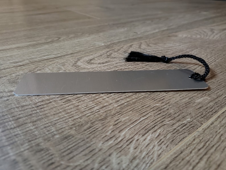 Puede incluir: Un marcap&aacute;ginas de metal plateado con un borla y un cord&oacute;n negros.