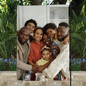 May include: A group of six people, including children, smiling and posing for a photo. They are standing in front of a white wall with a door behind them. The people are wearing casual clothing.