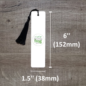 Puede incluir: Marcap&aacute;ginas blanco con un borla negra y el texto "Mortal Frog Gifts" en un c&iacute;rculo verde. El marcap&aacute;ginas mide 15,2 cm de alto y 3,8 cm de ancho.
