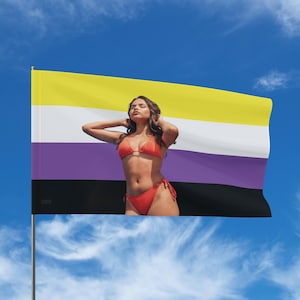 May include: A non-binary pride flag with yellow, white, purple, and black stripes is displayed against a blue sky. A person in a red bikini stands in front of the flag, with their arms raised.