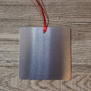 May include: A silver metal blank tag with a red ribbon attached to the top hole.