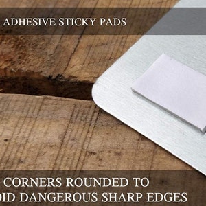 May include: Close-up of a silver metal sign with rounded corners and self-adhesive sticky pads on the back. The text "SELF ADHESIVE STICKY PADS" and "ALL CORNERS ROUNDED TO AVOID DANGEROUS SHARP EDGES" is printed on the sign.
