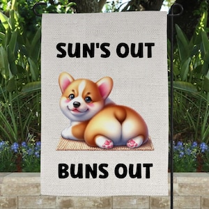May include: A white garden flag featuring a cartoon corgi dog with its rear end facing the viewer. The text "SUN'S OUT BUNS OUT" is printed on the flag.