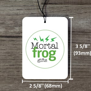 May include: A white rectangular air freshener with rounded corners, featuring the text "Mortal frog gifts" in black and green within a green circle. The air freshener measures 2 5/8 inches (68mm) wide and 3 5/8 inches (93mm) tall.