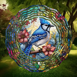 May include: A bluebird wind spinner with a blue and white bird perched on a branch with pink flowers. The wind spinner is made of metal and has a circular shape. The background is a blurred image of a garden.