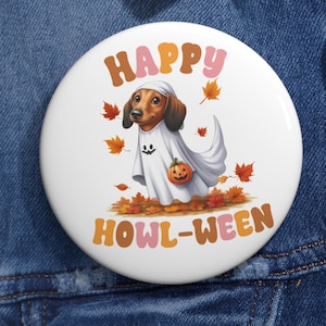 May include: A white badge with a dachshund in a ghost costume, carrying a pumpkin. The words "HAPPY HOWL-WEEN" are in orange and brown. The design includes autumn leaves, creating a Halloween theme.