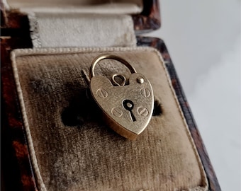 May include: A gold heart-shaped padlock charm with a keyhole and decorative details. The charm is displayed in a velvet-lined box.