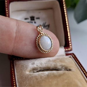 May include: A gold pendant featuring an oval opal gemstone. The opal is framed by a twisted rope design and set in a gold setting. The pendant is displayed in a red jewellery box.