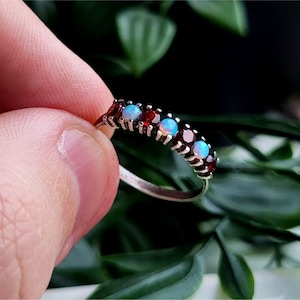 Könnte beinhalten: Ein silberner Ring mit abwechselnd roten und weißen Edelsteinen. Der Ring ist mit kleinen, runden Steinen besetzt.