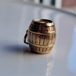 Può includere: Un ciondolo a forma di barile in metallo dorato con un design dettagliato a venature di legno. Il barile è un tema popolare per i gioielli ed è un'ottima aggiunta a qualsiasi braccialetto con ciondoli.