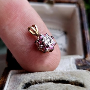 Può includere: Un ciondolo d'oro con un design a forma di fiore con pietre preziose rosa e bianche.