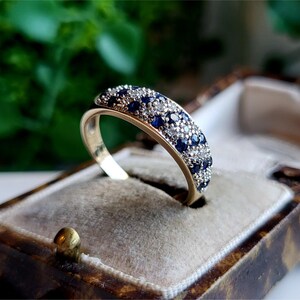 May include: A gold band ring with a row of blue sapphires and smaller white diamonds set in the metal.