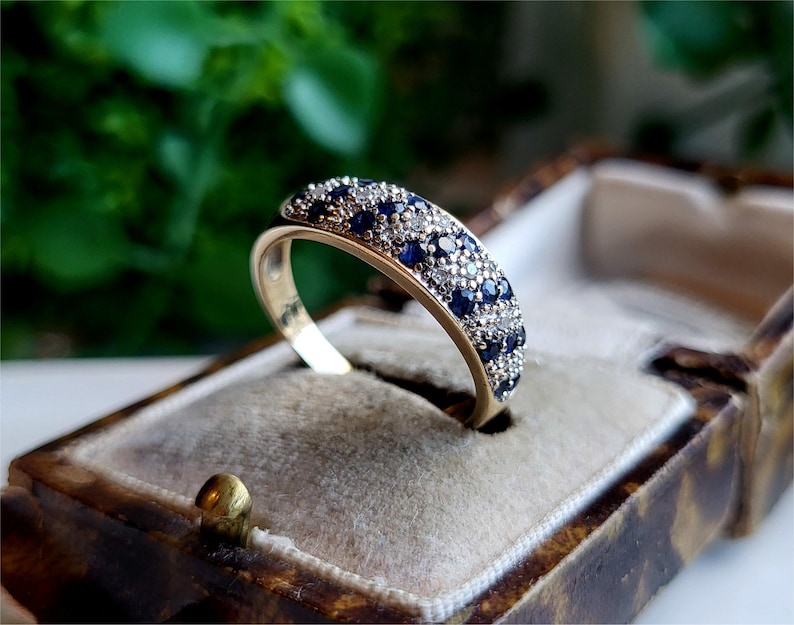 May include: A gold band ring with a row of blue sapphires and smaller white diamonds set in the metal.